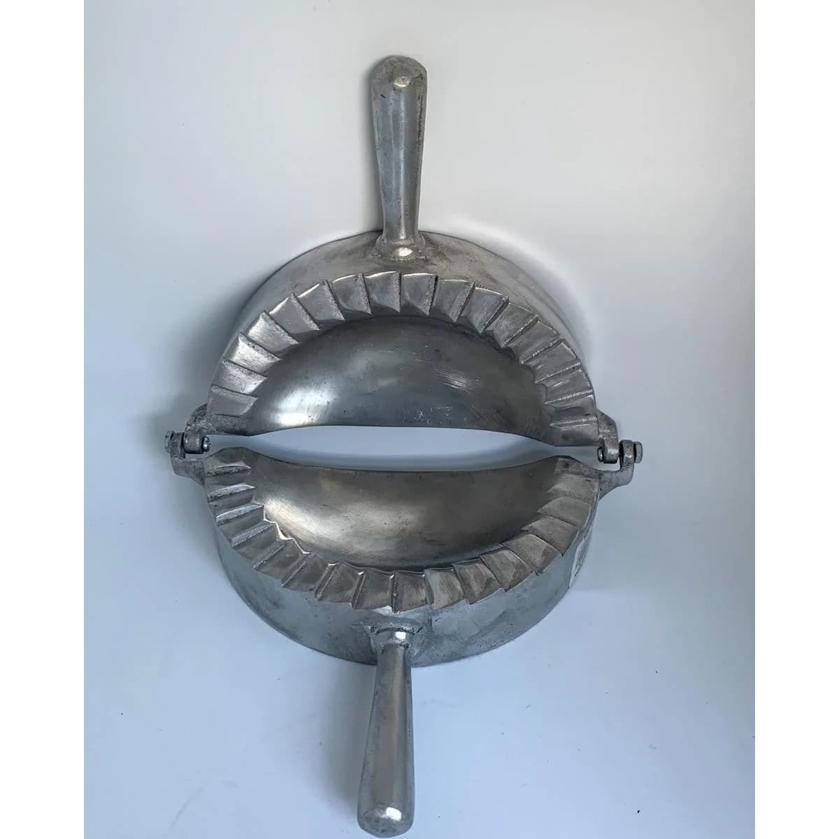 Molde manual de aluminio con bisagra para dar forma y sellar empanadas.