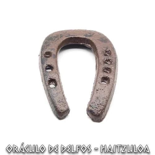 Herradura rústica de hierro pequeña con perforaciones para clavos.